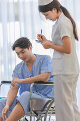 Obraz premium Asian professional young female nurse in white uniform holding clipboard writing note on paper while visiting monitoring asking male patient in blue hospital clothes sitting on wheelchair in ward
