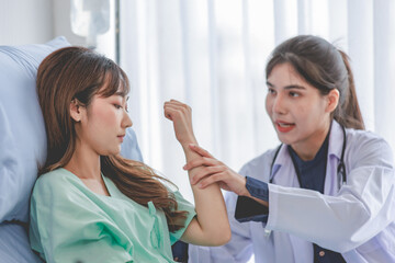 Asian young professional female practitioner doctor in white lab coat with stethoscope holding touching checking monitoring patient injury arm and muscle while laying down on bed in hospital wardroom
