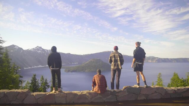 wide 4k establishing shot of a group of four 4 male friends looking out into the distance with crater lake oregon beneath them in slow motion