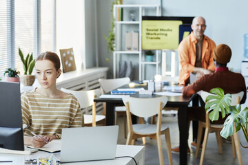 Group of young people working in office with focus on woman using computer i9n foreground, copy space