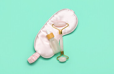 Facial massage tool with cosmetic dropper bottle and sleeping mask on green background