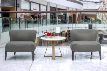 Two gray upholstered chairs and marble table with flower arrangement and white lamp. Modern interior design. Meeting area