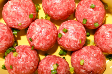 Raw meat balls with cut green onion on yellow background