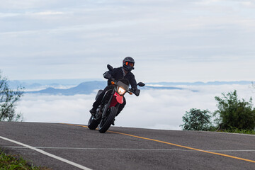 Motorcyclist riding a motorcycle on a paved road behind the sea of fog and mountain peaks, Mo Hin...