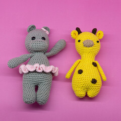 Amigurumi of hippo with tutu and giraffe with brown spots, on pink background.