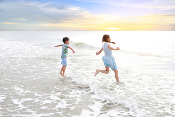 Fototapeta na wymiar Cheerful Asian young sister and little brother having fun together on tropical sand beach at sunrise. Happy family boy and girl enjoy in summer holiday.