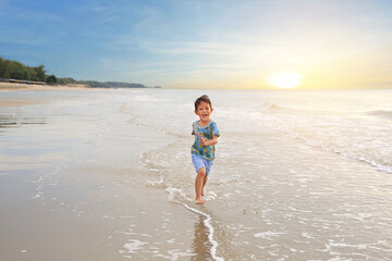 Fototapeta na wymiar Happy Asian little boy having fun running on tropical sand beach at sunrise.
