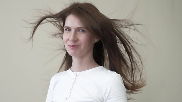 Portrait of a girl 35 years old with long brown hair and blue eyes on a beige background. Hair develops from exposure to a fan and wind. Slow motion
