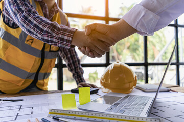 Engineers, architects, construction workers shake hands after project planning contract at desk in...