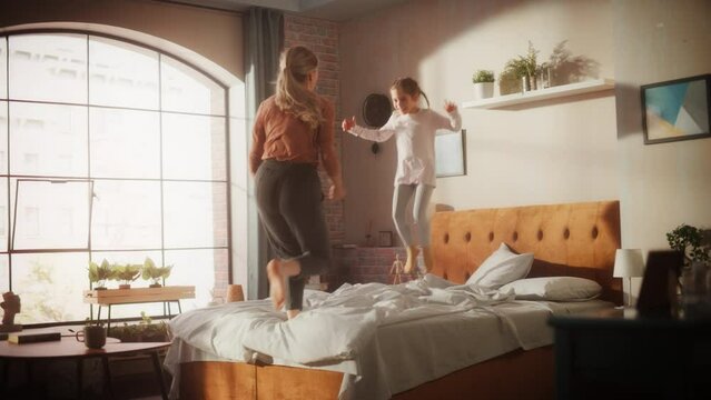 Mother and Small Daughter Having Fun at Home. Cheerfully Playing, Jumping on a Bed in Stylish Loft Apartment. Happy Childhood, Parenthood and Motherhood Memories. Slow Motion Footage.