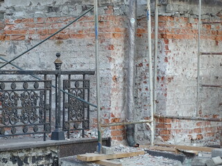 Horizontal full-color photo. Part of the wall of an old building. Crumbling brickwork surrounded by construction debris.