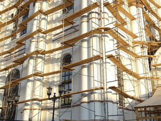 Full-color horizontal photo. Repair work to change the facade of the building. The high wall is covered with scaffolding.