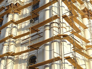 Full-color horizontal photo. Repair work to change the facade of the building. The high wall is covered with scaffolding.