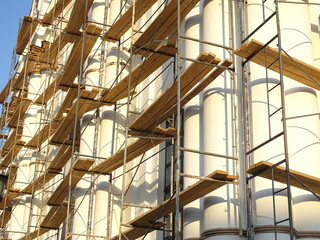 Full-color horizontal photo. Repair work to change the facade of the building. The high wall is covered with scaffolding.