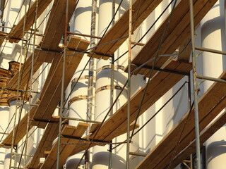 Full-color horizontal photo. Repair work to change the facade of the building. The high wall is covered with scaffolding.