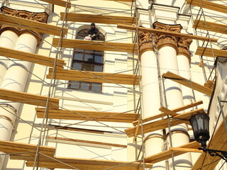 Full-color horizontal photo. Repair work to change the facade of the building. The high wall is covered with scaffolding.