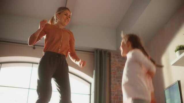 Close Up of a Mother and Small Daughter Having Fun at Home. Cheerfully Playing, Jumping on a Bed in Stylish Loft Apartment. Happy Childhood, Parenthood and Motherhood Memories. Slow Motion Footage.