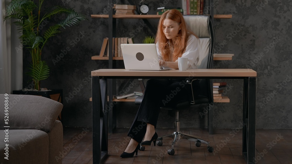 Sticker Caucasian red-haired woman typing on her laptop in a beautifully decorated office.