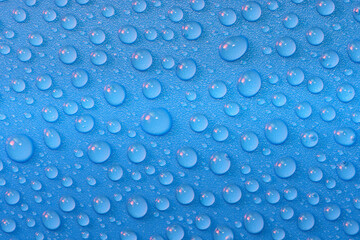 Water droplets with pink highlights on a shiny blue plastic surface fresh vibrant glittering appearance 