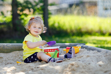 Cute toddler girl playing in sand on outdoor playground. Beautiful baby having fun on sunny warm...