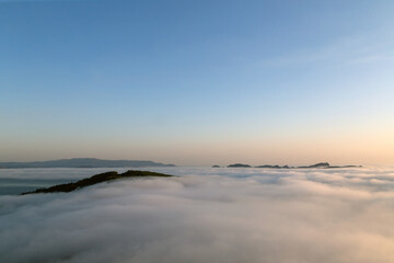 Paisaje costero cubierto por la niebla. Se puede distinguir sobresaliendo de la niebla Cabo Home y las Islas Cíes. Ría de Vigo, Galicia, España. - obrazy, fototapety, plakaty