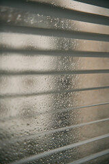 Close-up of rainy water droplets and glass windows with blinds. Macro shot of raindrops on a glass. Window blinds with water drops.