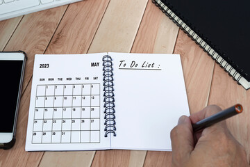 Hands with pen writing to do list with May 2023 calendar on notebook.