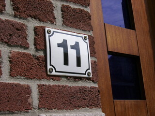 House sign number 11: square white plaque with black figures against a brick wall