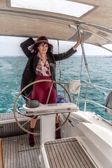 Attractive middle-aged woman at the helm of a yacht on a summer day. Luxury summer adventure, outdoor activities.