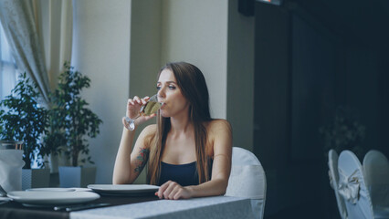 Pretty young woman is sitting alone at table in restaurant, drinking champagne and waiting for her...