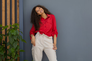 Young woman in red shirt standing against grey and wooden wall