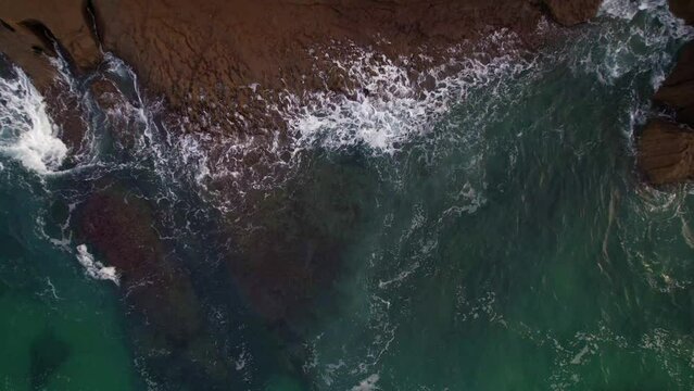 aerial top view of constrast waves forming and abrupt rocks of the cantabrian coast, in Isla, a village of Cantabria, Spain. Drone aerial top up shoot