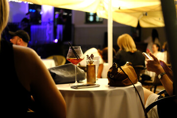 Atmosphere of an evening cafe. There is a cocktail on the table, the girl sits with her back to the camera and listens to music
