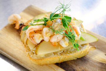 Bruschetta with shrimp, pear and pine nuts on a wooden board