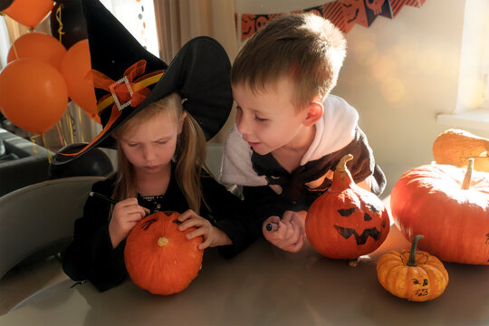 Brother and sister in carnival costumes painting pumpkins for Halloween