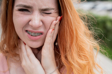 Young red-haired woman with braces suffering from pain. 