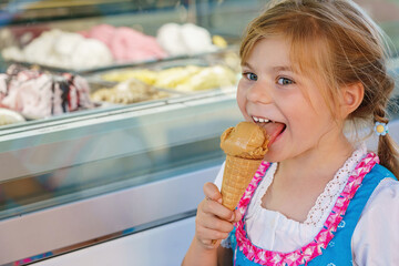 Little preschool girl eating sweet ice cream in waffle cone on sunny summer day. Happy toddler child eat icecream dessert. Sweet food on hot warm summertime days - obrazy, fototapety, plakaty