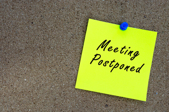 Meeting postponed on yellow stick note and pinned to a cork notice board.