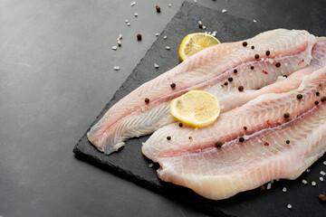 Raw pangasius fish fillet with lemon and spice on state plate on concrete background