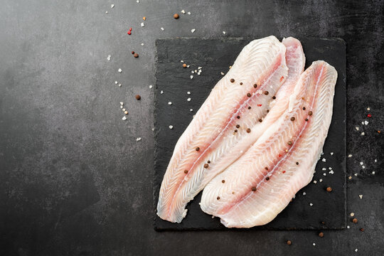 Raw pangasius fish fillet with lemon and spice on state plate on concrete background