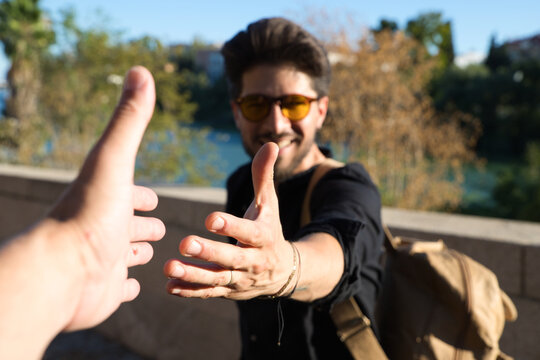 Handsome young man with yellow sunglasses is shaking hands with a friend to greet him. The man is happy and smiling. Concept friendship and empathy.