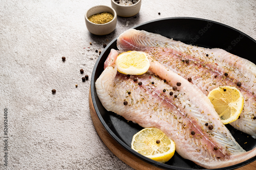 Wall mural Raw pangasius fish fillet with lemon and spice in frying pan on concrete background