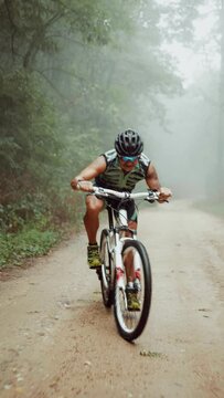 Vertical shot of a cyclist climbing a dirt road in the forest on a cloudy and rainy day