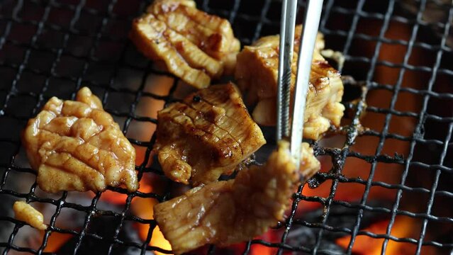 網の上で焼かれる味付けされた牛ミノ。炭火の強火力で加熱され、表面がこんがりと焼き上がりながら煙が上がる様子を至近距離で捉えたクローズアップ映像。飲食店メニュー、焼肉店、肉料理の紹介、スタミナ料理をテーマにした広告や映像素材に。 | Close-up of seasoned beef tripe being grilled on a charcoal brazier.