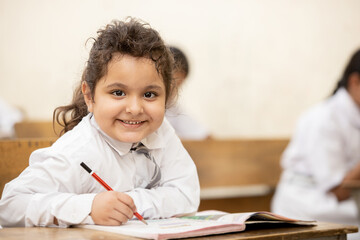 Portrait of happy indian schoolgirl sitting at desk in classroom, school kids with pens and notebooks writing test Elementary school, Education concept.
