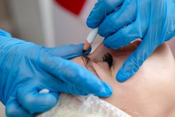 Closeup of An Eye of Caucasain Female During Tattoo Facial Markings Using Black makeup Pencil During Professional Eyebrow Permanent Makeup in Salon.