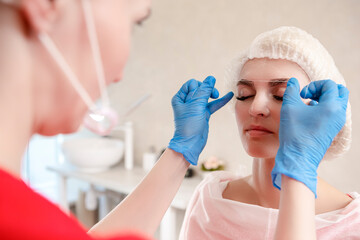 Naklejka premium Tattoo Concepts. Markup with White Facial Thread On Eyebrows of Young Caucasian Woman During a Process of Permanent make up in Salon