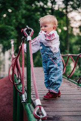 A little girl in an embroidered shirt and denim jumpsuit plays on the playground