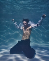 Fototapeta na wymiar young man in a white shirt and trousers underwater in the pool