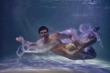 Fototapeta na wymiar young man in white ribbons and trousers underwater in the pool on a dark background
